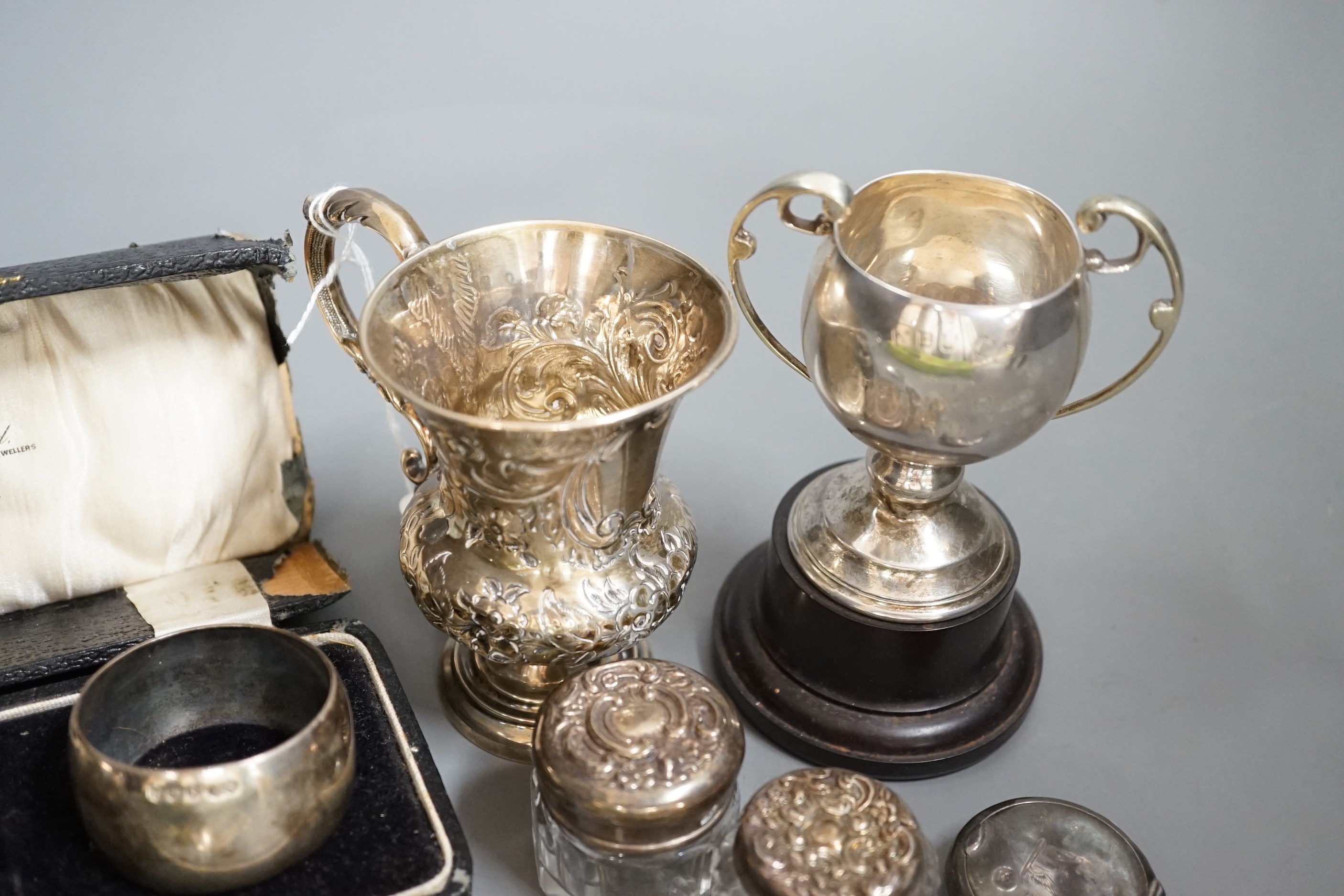 A Victorian repousse silver christening mug, Birmingham, 1861, 9.5cm, a cased pair of silver napkin rings, four assorted silver mounted toilet jars, a silver compact, small silver trophy cup and a silver caddy spoon.